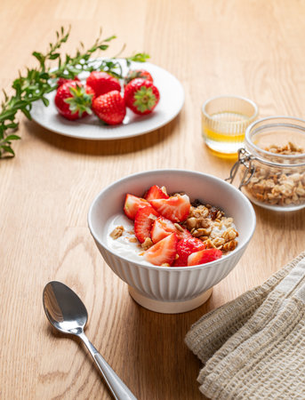 Granola or muesli with natural greek yogurt, strawberry and honey in a bowl on a wooden background with berries and sunlight. Healthy and nutritious breakfast concept for advertising menu cafe or banner. Copy space.の写真素材
