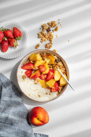 Granola or muesli with natural greek yogurt, strawberry and peach in a bowl on a white background...