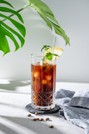 Cold brew coffee tonic in a glass with lemon and ice on a light background with coffee beans,...
