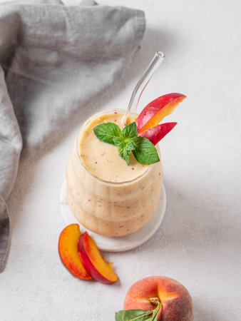 Smoothie with peach and banana in a glass on a light background with tropical fruits and napkin. Healthy eating and detox diet concept for advertising menu or banner cafe. Top view, copy space.の写真素材