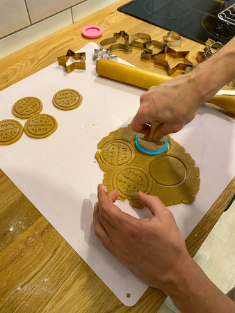 Hands pressing cookie stamp onto dough with cookie cutters and rolling pin on wooden kitchen...