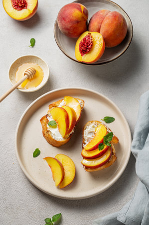 Toast bruschetta with peach, nectarine, cream cheese or ricotta and honey on a plate on a light background with fresh fruits and mint. Healthy summer snack concept. Top view.の写真素材