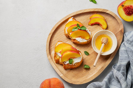 Toast bruschetta with peach, nectarine, cream cheese or ricotta and honey on a wooden plate on a light background with fresh fruits and napkin. Healthy summer snack concept. Top view, copy space.の写真素材