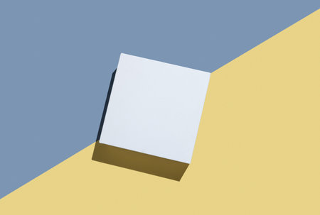 White cube, podium or box with shadow on diagonally divided yellow and blue background. Concept abstract geometric design for advertising or product demonstration. Top view, copy space.の写真素材