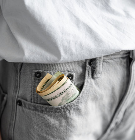 Rolled up US dollar bills sticking out of front pocket of jeans on casual clothing background close up. Personal finance concept.の写真素材