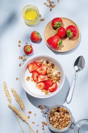 Granola or muesli with natural greek yogurt, strawberry and honey in a bowl on a blue background with berries and shadows. Healthy and nutritious breakfast concept for advertising menu cafe or banner. Top view.の写真素材