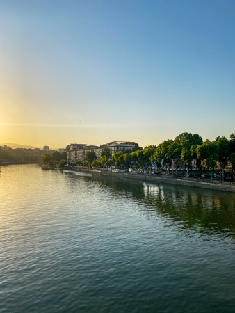 Calm cityscape on the river bank with trees, buildings and calm water under clear blue sky at sunset, capturing peaceful urban nature. Tbilisi, Georgia.の写真素材