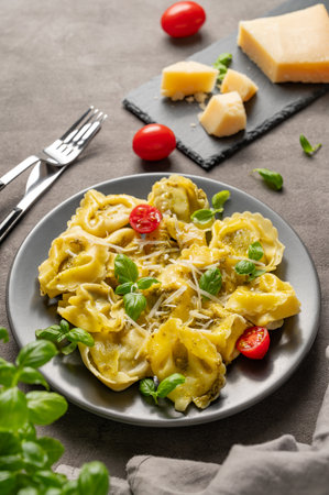 Tortellini pasta with parmesan, pesto and basil in a plate on a dark background with cheese, herb and tomato. Traditional Italian homemade food concept in rustic style. Copy space.の写真素材