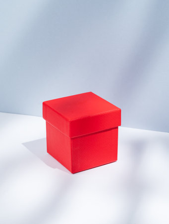 Red box on a white and blue background with soft shadows. Concept of a gift for a holiday, a surprise or a sign of attention to a close loved one. Front view, copy space.の写真素材