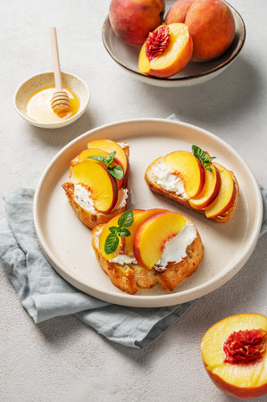 Toast bruschetta with peach, nectarine, cream cheese or ricotta and honey on a plate on a light background with fresh fruits and mint. Healthy summer snack concept. Top view.の写真素材