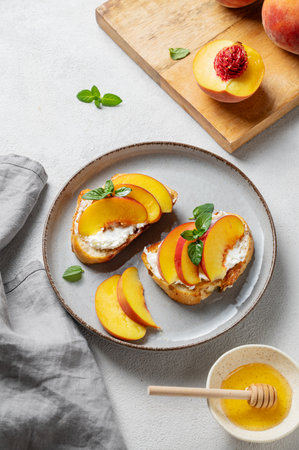 Toast bruschetta with peach, nectarine, cream cheese or ricotta and honey on a plate on a light background with fresh fruits and mint. Healthy summer snack concept. Top view.の写真素材