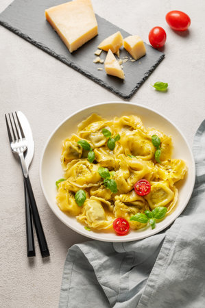Tortellini pasta with parmesan, pesto and basil in a plate on a light  background with tomato, cheese and cutlery. Traditional Italian homemade food concept. Top view.の写真素材