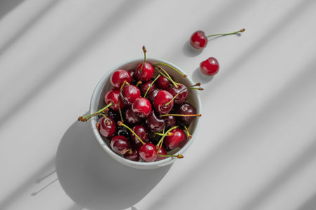 Bowl with fresh red cherry on white background with sunny light and shadows. Summer and healthy food...