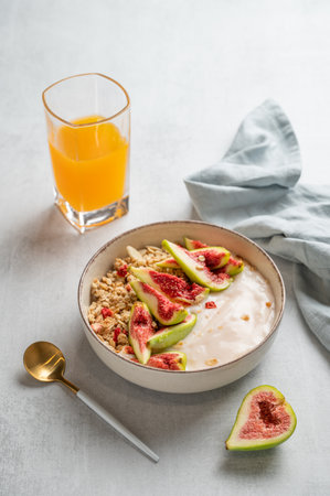Natural yogurt with granola, figs and honey in a bowl on a light background with glass of orange juice, spoon and fruits. Concept of healthy and nutritious detox food for breakfast. Top view.の写真素材