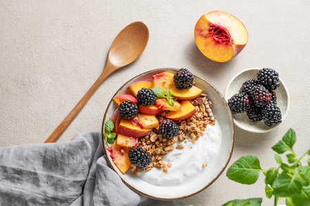 Natural Greek yogurt with granola or muesli, peach and blackberry in a bowl on a light background with fresh fruits and berries. Concept of healthy and nutritious detox food for breakfast. Top view, copy space.の写真素材
