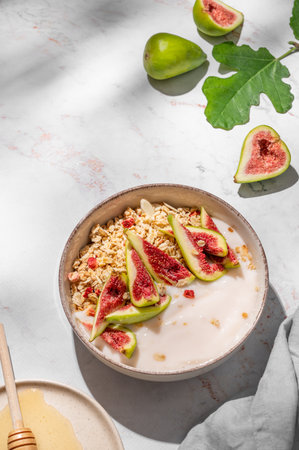 Natural yogurt with muesli, figs and honey in a bowl on a marble background with fruits and morning shadows. Concept of healthy and nutritious detox food for breakfast. Top view, copy space.の写真素材