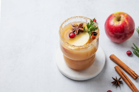 Apple cider with cinnamon, anise, brown sugar and rosemary in a glass on a light background with...