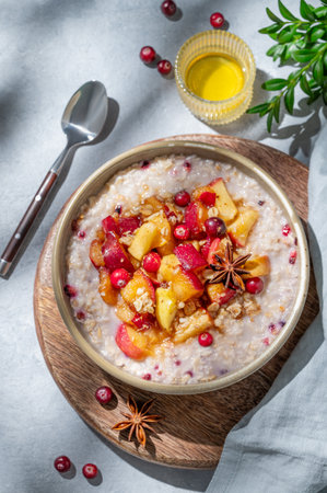 Overnight oatmeal with apples, cranberries, and cinnamon in a bowl on a wooden board on a blue background with honey and shadows. Concept for a healthy vegan meal or breakfast snack. Top view.の写真素材