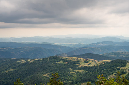 Extensive view of green forested mountains and valleys under gloomy cloudy sky on natural scenic...