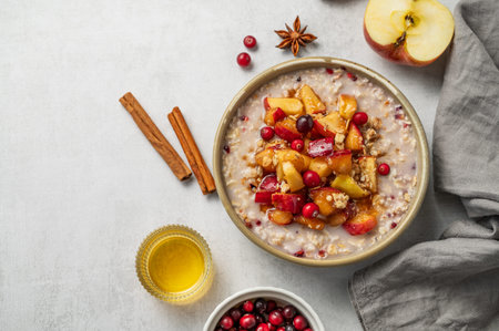 Overnight oatmeal with apples, cranberries, and cinnamon in a bowl on a light background with honey and berries. Concept for a healthy vegan meal or breakfast snack. Top view, copy space.の写真素材