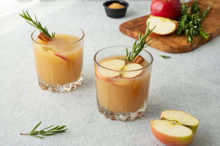 Hot apple cider with cinnamon, anise, and rosemary in glasses on a light background with fresh fruits. Concept a traditional, spicy, warming drink for fall and winter.の写真素材