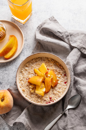 Oatmeal with peaches and nuts  in a bowl on a light background with honey, glass of orange juice, spoon and fresh fruit. Concept for a healthy vegan dish or breakfast snack. Top view, copy space.の写真素材