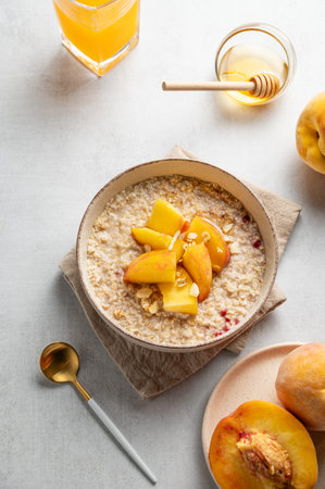 Oatmeal with peaches and nuts  in a bowl on a light background with honey, glass of orange juice, spoon and fresh fruit. Concept for a healthy vegan dish or breakfast snack. Top view, copy space.の写真素材
