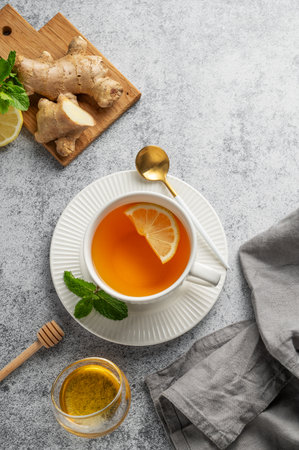 Tea with lemon, ginger, honey, and mint in a cup on a gray background with citrus fruits, herbs and napkin. Concept of a hot drink to support immunity and health during the cold season. Top view, copy space.の写真素材