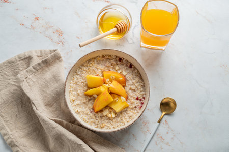 Oatmeal with peaches and nuts  in a bowl on a marble background with honey, glass of orange juice, spoon and napkin. Concept for a healthy vegan dish or breakfast snack. Top view, copy space.の写真素材
