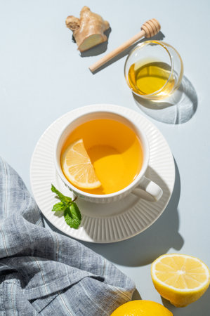 Hot tea with lemon, ginger, honey, and mint in a cup on a blue background with napkin and shadows. Concept of a drink to support immunity and health during the cold season. Top view, copy space.の写真素材