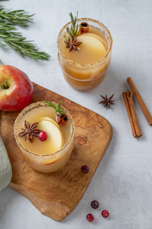 Apple cider with cinnamon, anise, brown sugar and rosemary on a wooden board on a light background with fresh fruits, cranberry and herb. Concept a traditional, spicy, warming drink for fall and winter. Top view.の写真素材