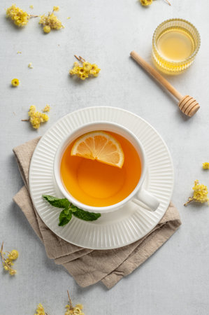 Hot tea with lemon, honey, and mint in a cup on a light background with dry flowers. Concept of a drink to support immunity and health during the cold season. Top view, copy space.の写真素材