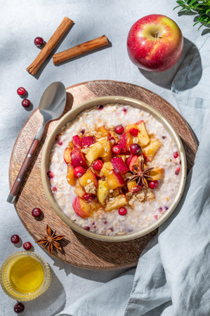 Overnight oatmeal with apples, cranberries, and cinnamon in a bowl on a wooden board on a blue background with honey and shadows. Concept for a healthy vegan meal or breakfast snack. Top view.の写真素材