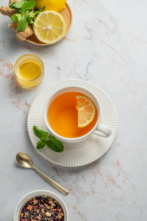 Tea with lemon, ginger, honey, and mint in a cup on a marble background with citrus fruits and herbs. Concept of a hot drink to support immunity and health during the cold season. Top view, copy space.の写真素材