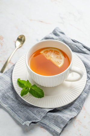 Hot tea with lemon and mint in a cup on a marble background with spoon and napkin. Concept of a drink to support immunity and health during the cold season. Top view, copy space.の写真素材
