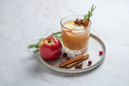 Hot apple cider with cinnamon, anise, and rosemary in glass on a marble background with cranberry,...