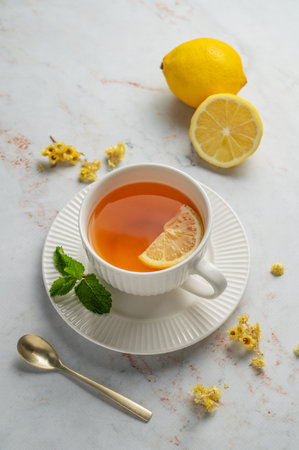 Tea with lemon and mint in a cup on a marble background with citrus fruits and dry flowers. Concept of a hot drink to support immunity and health during the cold season. Top view, copy space.の写真素材