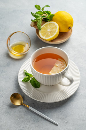 Hot tea with lemon, ginger, honey, and mint in a cup on a light background with citrus fruits and herbs. Concept of a drink to support immunity and health during the cold season. Copy space.の写真素材