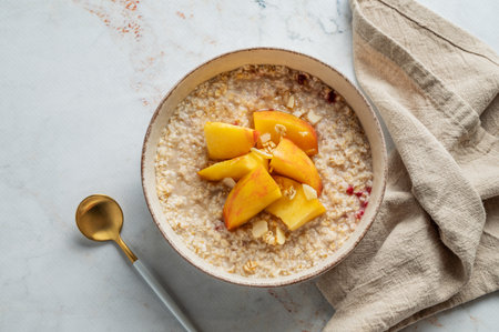 Oatmeal with peaches and nuts  in a bowl on a marble background with honey, spoon and napkin. Concept for a healthy vegan dish or breakfast snack. Top view, copy space.の写真素材