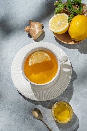 Hot tea with lemon, ginger, honey, and mint in a cup on a blue background with citrus fruits and morning shadows. Concept of a drink to support immunity and health during the cold season. Top view, copy space.の写真素材