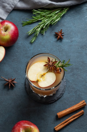 Hot apple cider with cinnamon, anise, and rosemary in glass on a dark blue background with fresh fruits and herb. Concept a traditional, spicy, warming drink for fall and winter. Top view, copy space.の写真素材