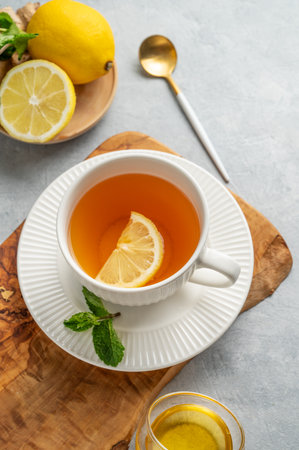 Hot tea with lemon, ginger, honey, and mint in a cup on a wooden board on a light background with citrus fruits. Concept of a drink to support immunity and health during the cold season. Top view, copy space.の写真素材