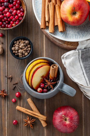 A cup of red mulled wine with spices, orange, apple slices and cranberry on a wooden background with cinnamon sticks and berries close up. A traditional autumn or Christmas drink concept for the holidays. Top view.の写真素材