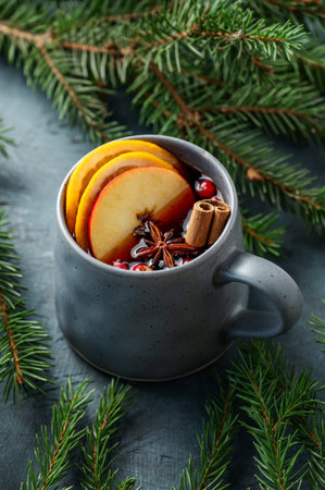 A cup of red mulled wine with spices, orange, apple slices and cranberry on a dark background with fir branch close up. A traditional autumn or Christmas drink concept for the holidays. Top view.の写真素材