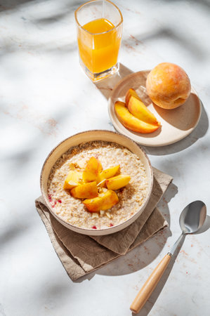 Oatmeal with peaches and nuts  in a bowl on a marble background with honey, glass of orange juice and shadows. Concept for a healthy vegan dish or breakfast snack. Top view, copy space.の写真素材