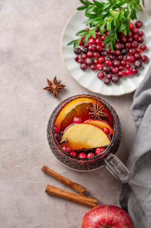A cup of red mulled wine with spices, orange, apple slices and cranberry on a light background with cinnamon sticks and beries. A traditional autumn or Christmas drink concept for the holidays. Top view, copy space.の写真素材