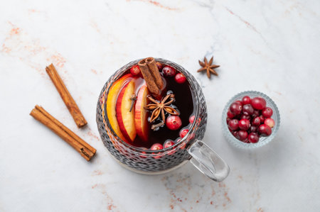 A cup of hot mulled wine with spices, orange and apple slices on a marble background with cinnamon sticks and cranberry. A traditional autumn or Christmas drink concept for the holidays. Top view, copy space.の写真素材