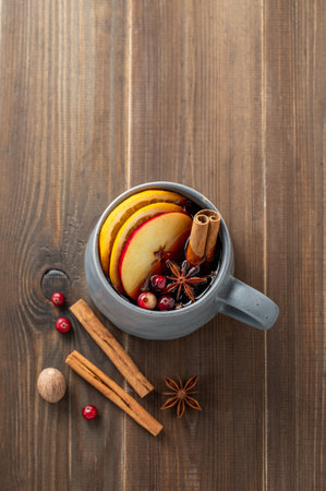 A cup of red mulled wine with spices, orange, apple slices and cranberry on a wooden background with cinnamon sticks. A traditional autumn or Christmas drink concept for the holidays in rustic style. Top view, copy space.の写真素材