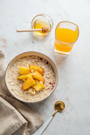 Oatmeal with peaches and nuts  in a bowl on a marble background with honey, glass of orange juice, spoon and napkin. Concept for a healthy vegan dish or breakfast snack. Top view, copy space.の写真素材