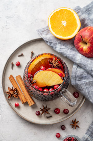 A cup of red mulled wine with spices, orange and apple slices on a light background with cinnamon sticks, cranberry and napkin. A traditional autumn or Christmas drink concept for the holidays. Top view, copy space.の写真素材